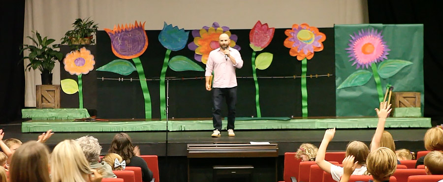 Scott Cohn on stage with Daddy Sat on a Duck during a school visit, children raising hands